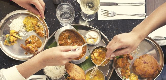 Close-up of people&#039;s hands taking food from several bowls of Indian food